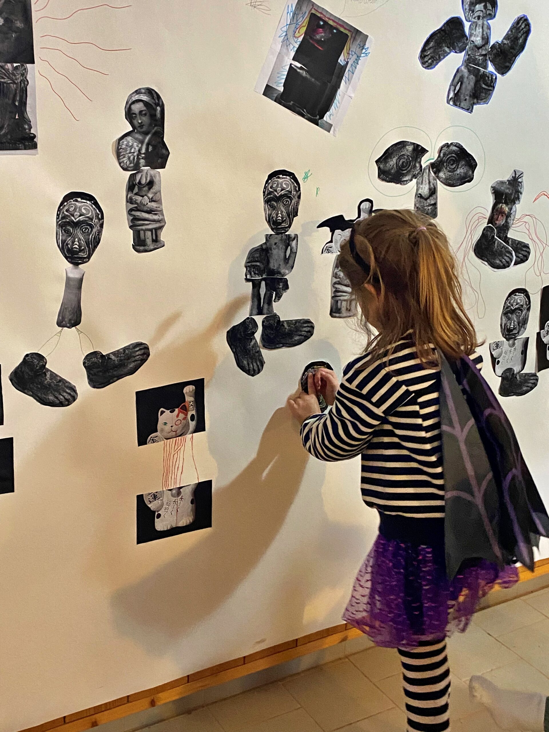 Vue d'une petite fille de dos qui colle des images sur un mur blanc - Agrandir l'image, fenêtre modale